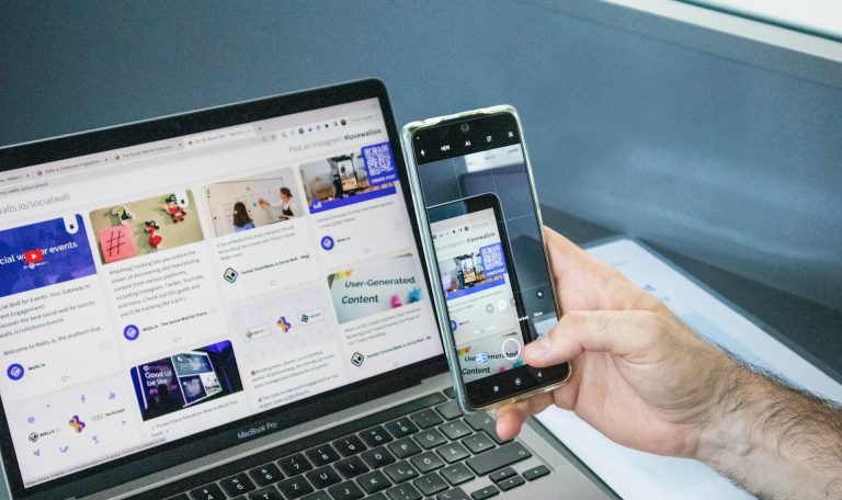a-man-holding-two-cell-phones-next-to-a-laptop