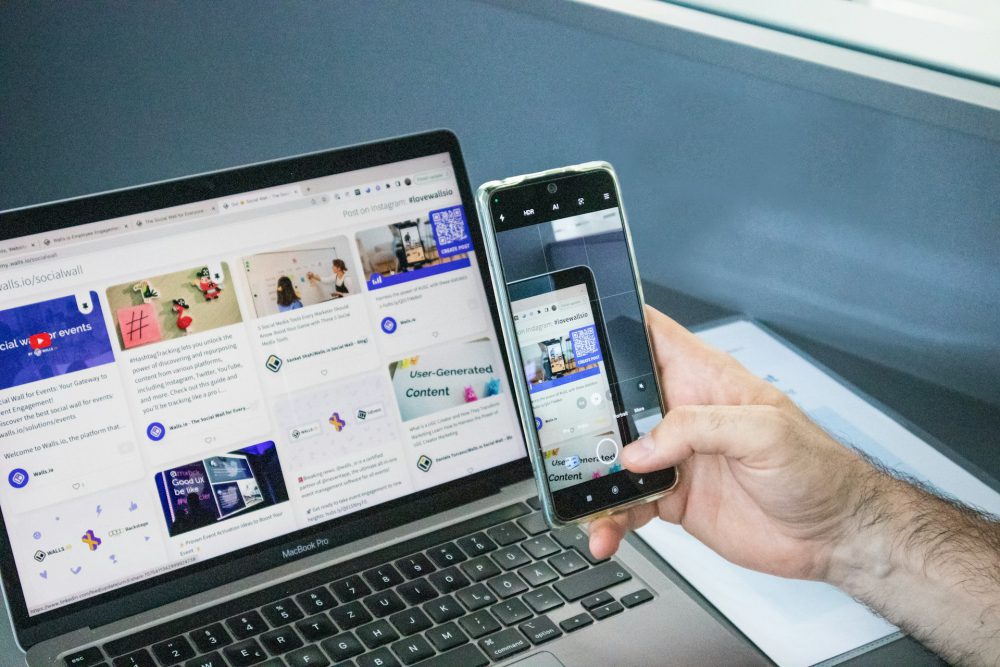 a-man-holding-two-cell-phones-next-to-a-laptop
